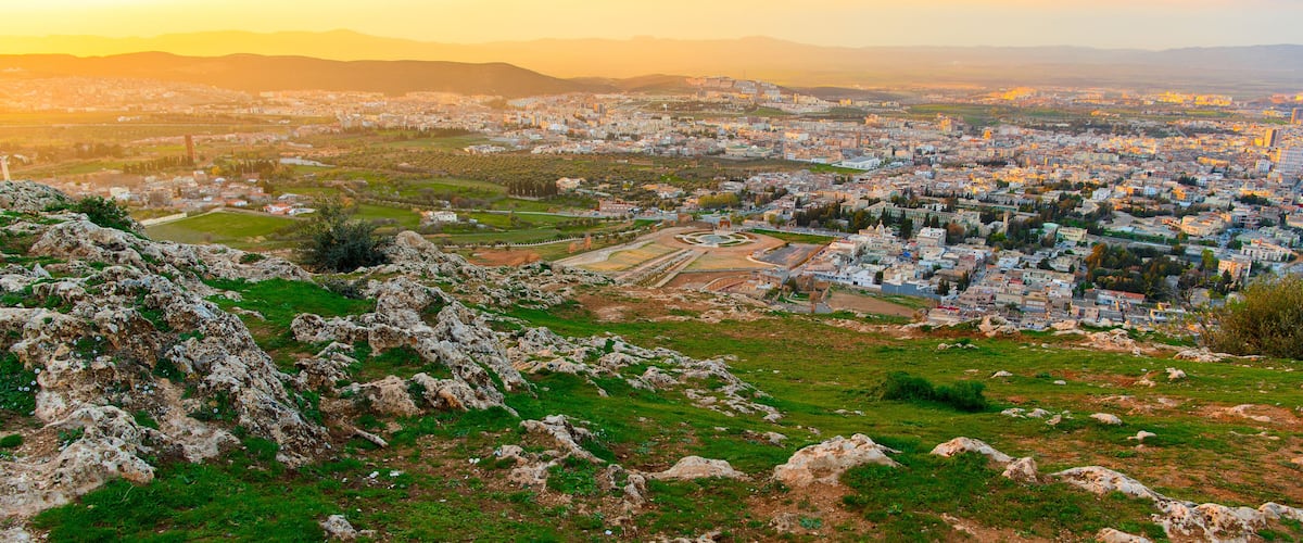 A cityscape with a prominent hill in the foreground and a view of the city extending towards the horizon.