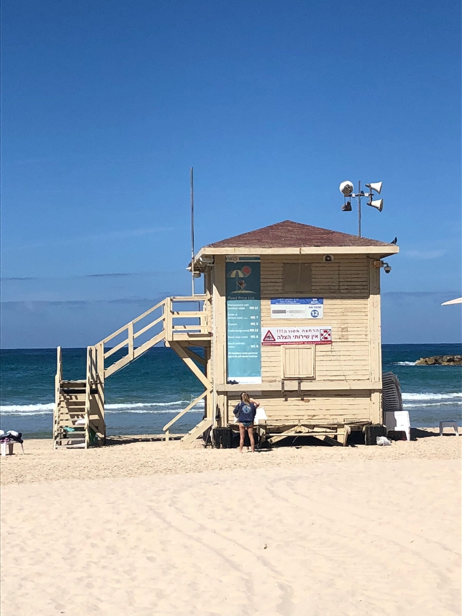 A wooden lifeguard tower with a staircase on a sandy beach, overlooking the ocean.