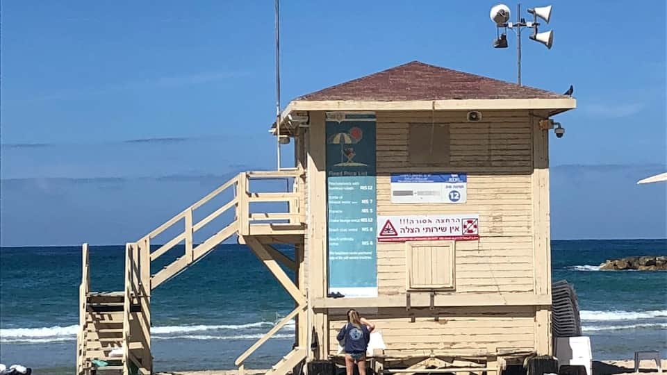 A wooden lifeguard tower with a staircase on a sandy beach, overlooking the ocean.