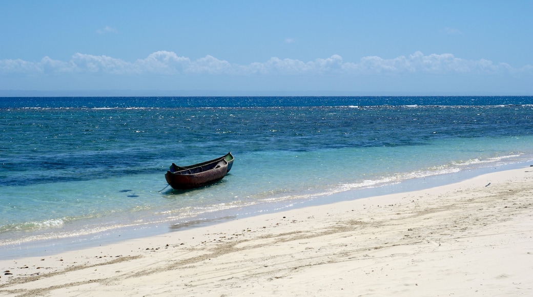 A boat on a sandy beach with clear blue water and a calm sea.