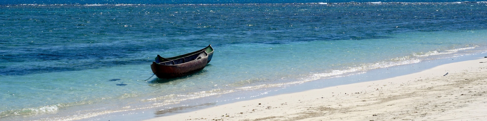 Una embarcación en una playa arenosa con agua azul cristalina y un mar en calma.