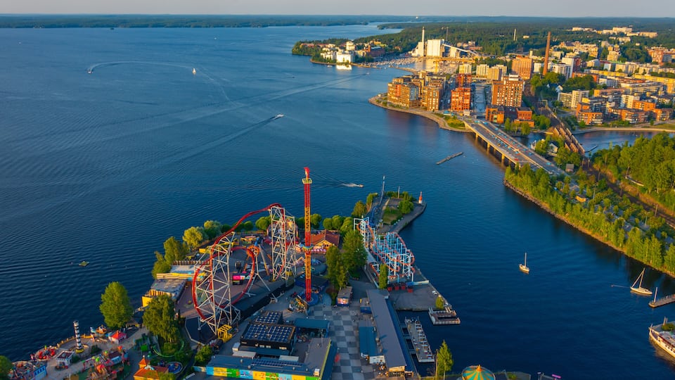 An amusement park with roller coasters and a Ferris wheel by a waterfront.