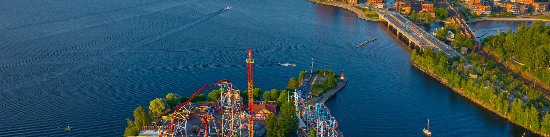 Parque de atracciones con montañas rusas y noria frente al agua.