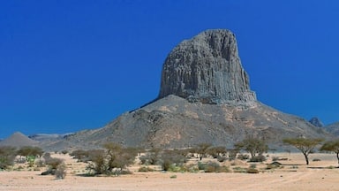 A desert landscape with a prominent rock formation and sparse vegetation.