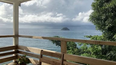 A wooden bench overlooking a calm sea with a small island in the distance and lush greenery on the right.