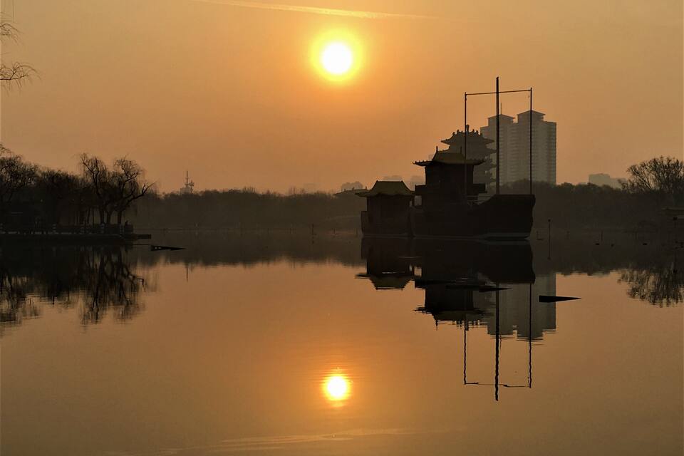 Un riu tranquil amb un vaixell i edificis tradicionals que reflecteixen el sol ponent.