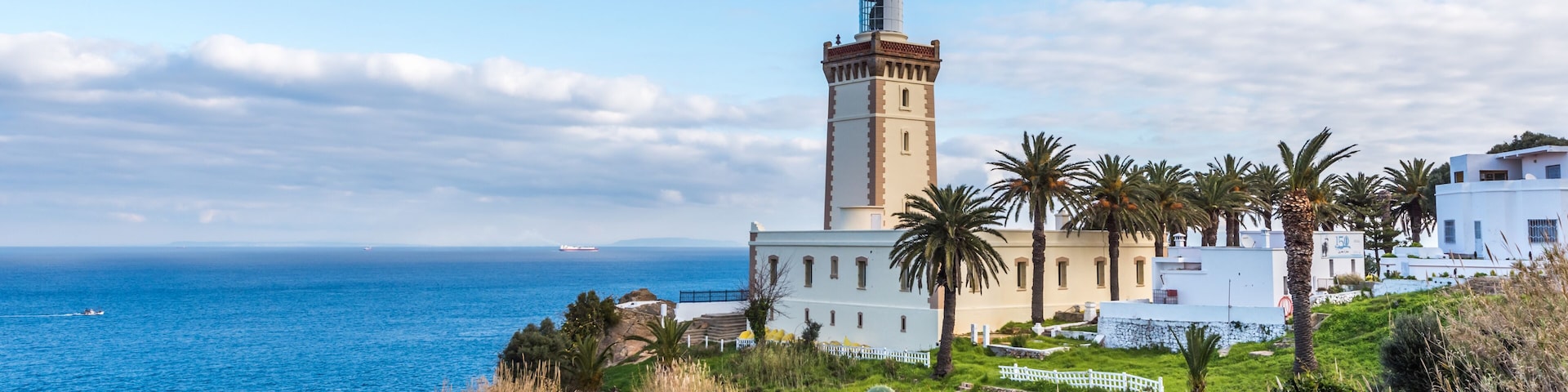 Un paysage côtier avec un phare, des bâtiments blancs et un cactus au premier plan.