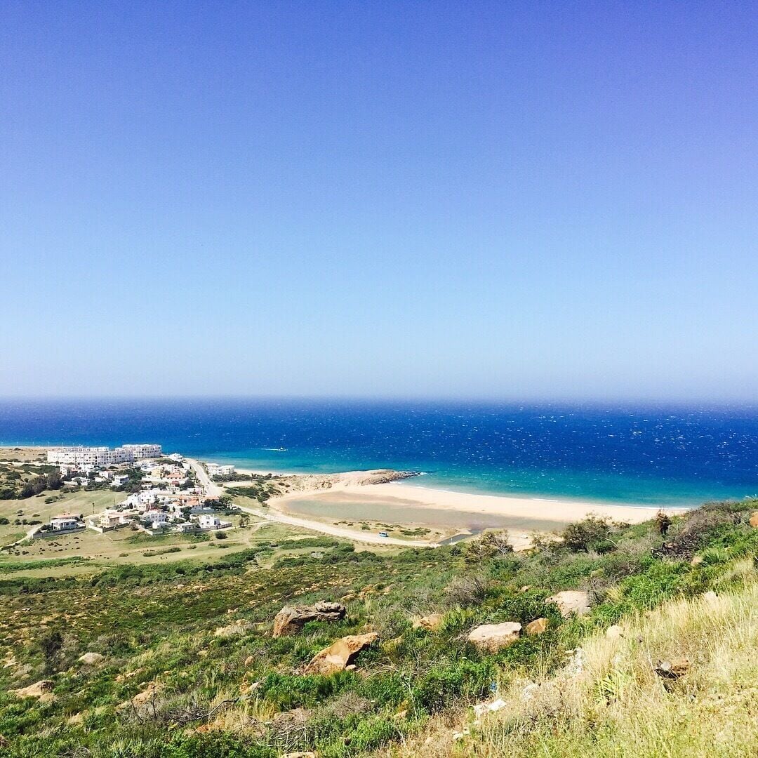 A coastal landscape with a beach, a small settlement, and a clear blue sky.
