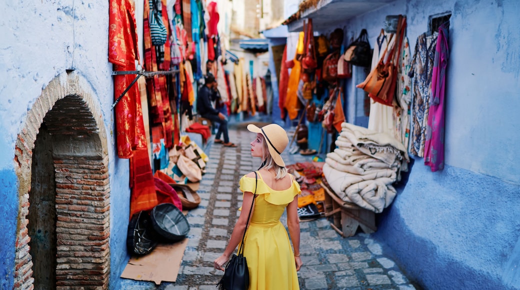Colorful traveling by Morocco. Young woman in yellow dress walking in medina of blue city Chefchaouen.