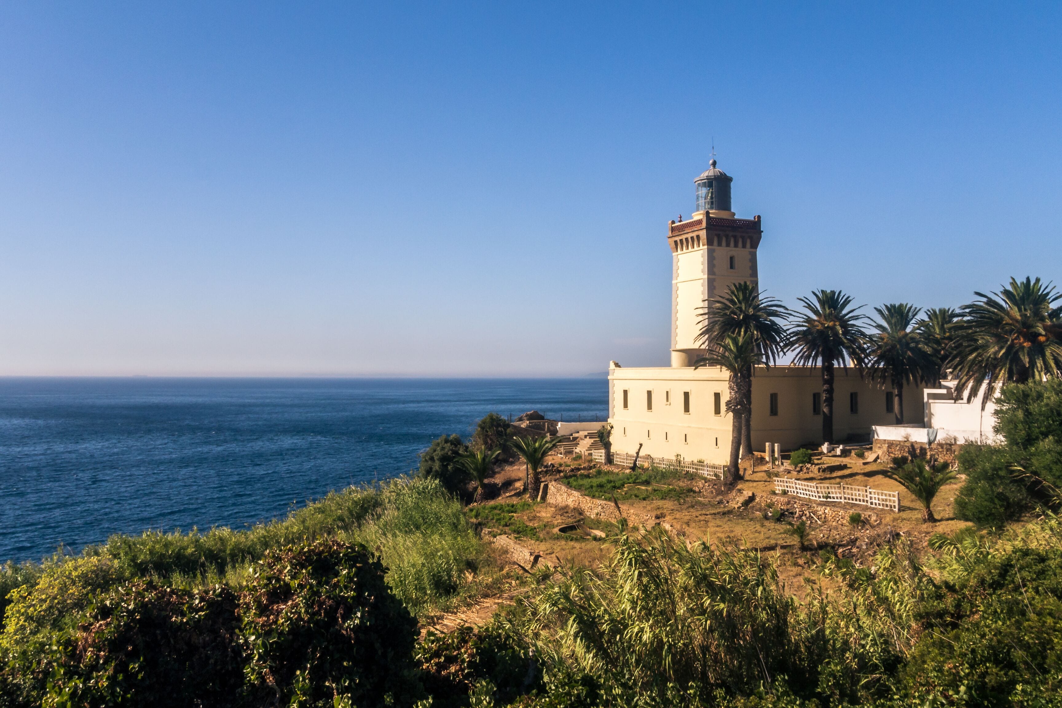 Um farol costeiro com vista ampla do oceano, rodeado por palmeiras e vegetação.