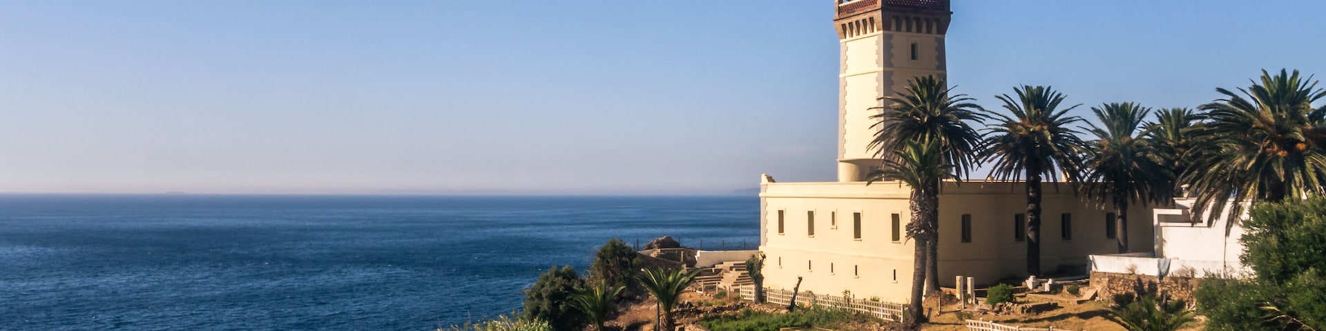 Um farol costeiro com vista ampla do oceano, rodeado por palmeiras e vegetação.