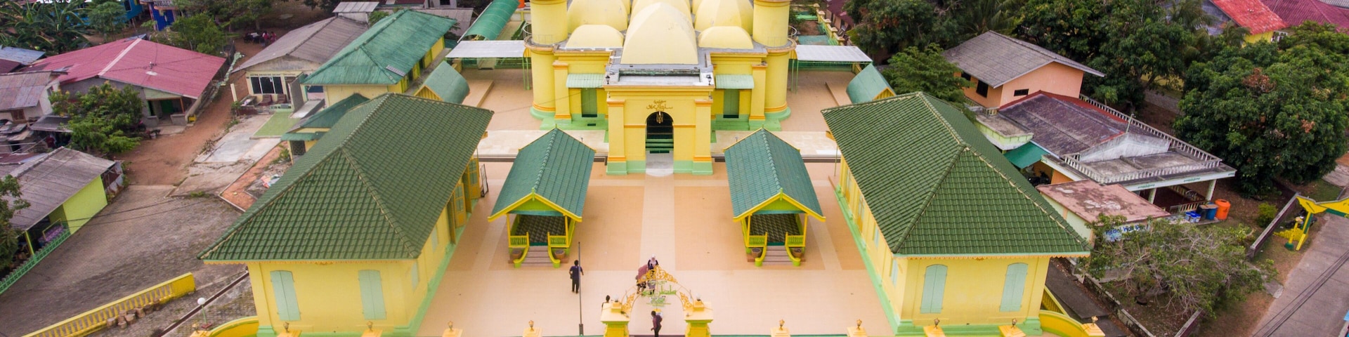 Un templo grande y amarillo con múltiples agujas y techos verdes, rodeado de exuberante vegetación y edificios más pequeños.