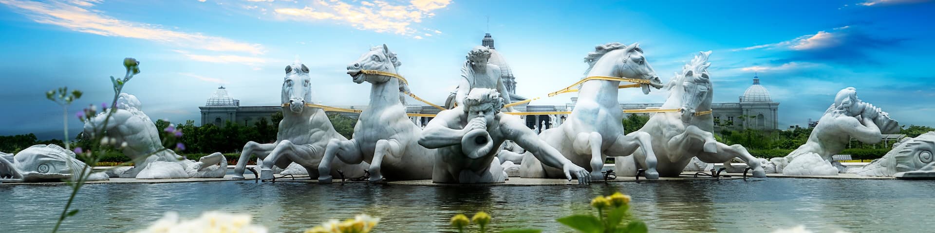 A sculpture of horses and riders in a fountain, with a clear sky and domed buildings in the background.