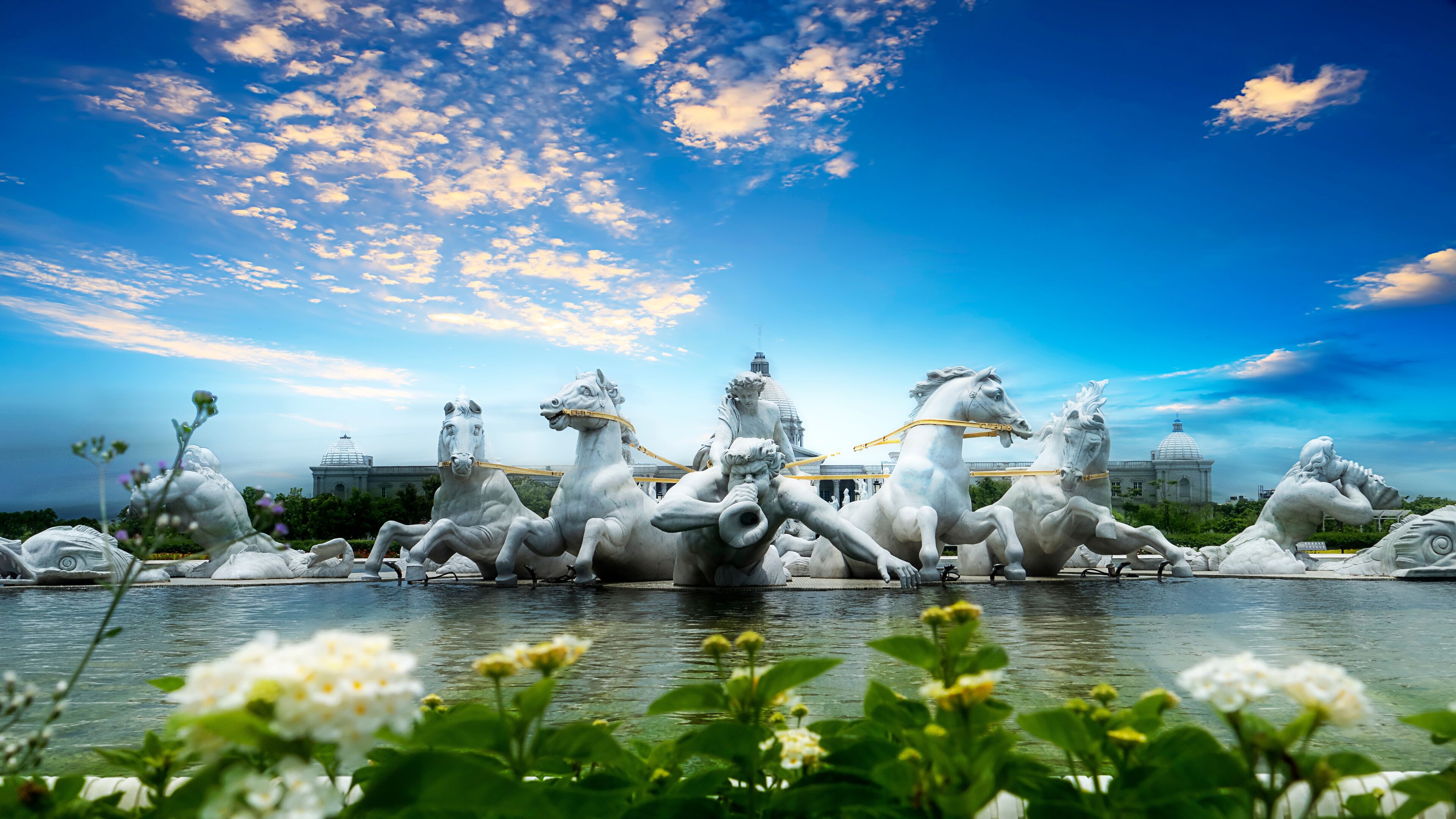 A sculpture of horses and riders in a fountain, with a clear sky and domed buildings in the background.