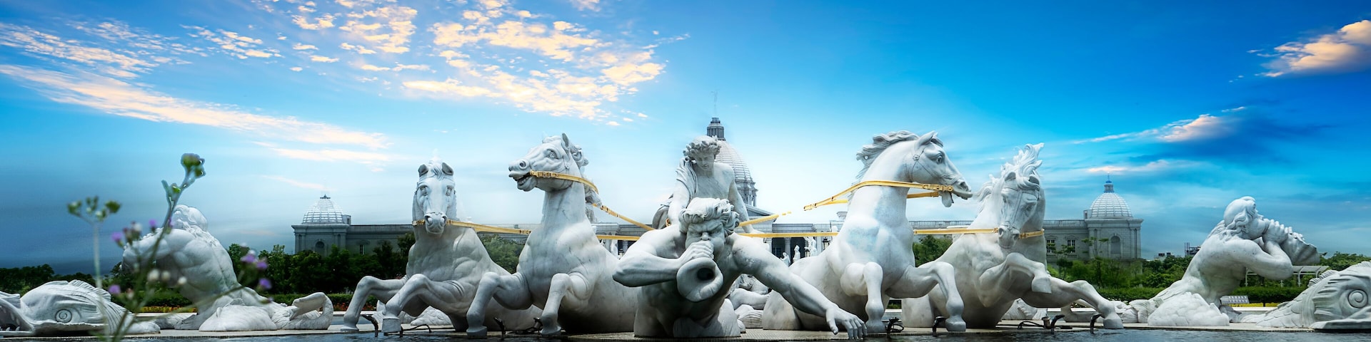 A sculpture of horses and riders in a fountain, with a clear sky and domed buildings in the background.