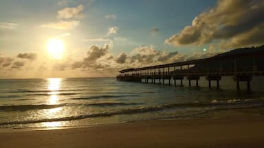 Une plage avec une jetée qui s’avance dans l’océan au coucher du soleil.