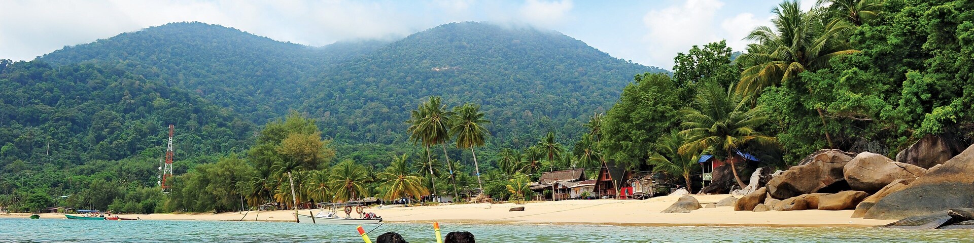 Uma praia com águas cristalinas, palmeiras e uma montanha ao fundo.