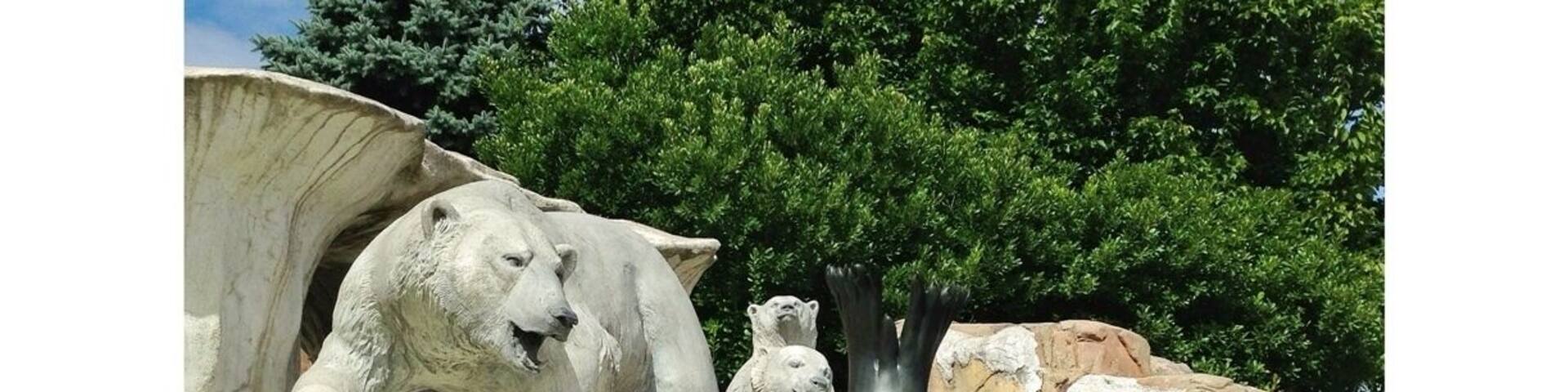 A polar bear and a seal in a zoo enclosure with rocky terrain and trees in the background.
