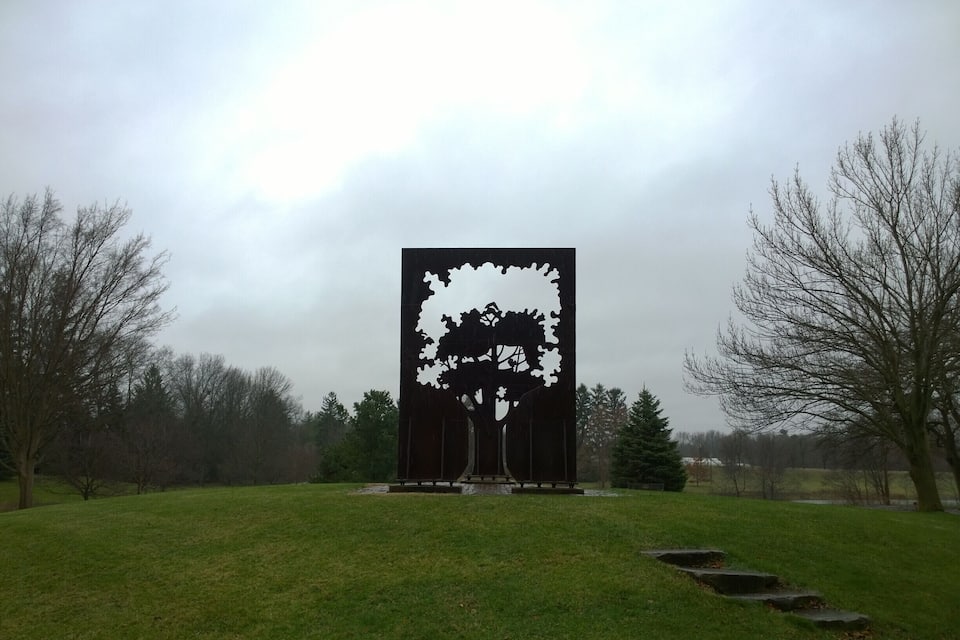 Una gran escultura negra d'un arbre en un parc amb gespa i altres arbres sense fulles al voltant.