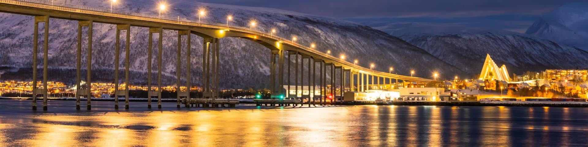 A bridge spanning a body of water with snow-covered mountains in the background.