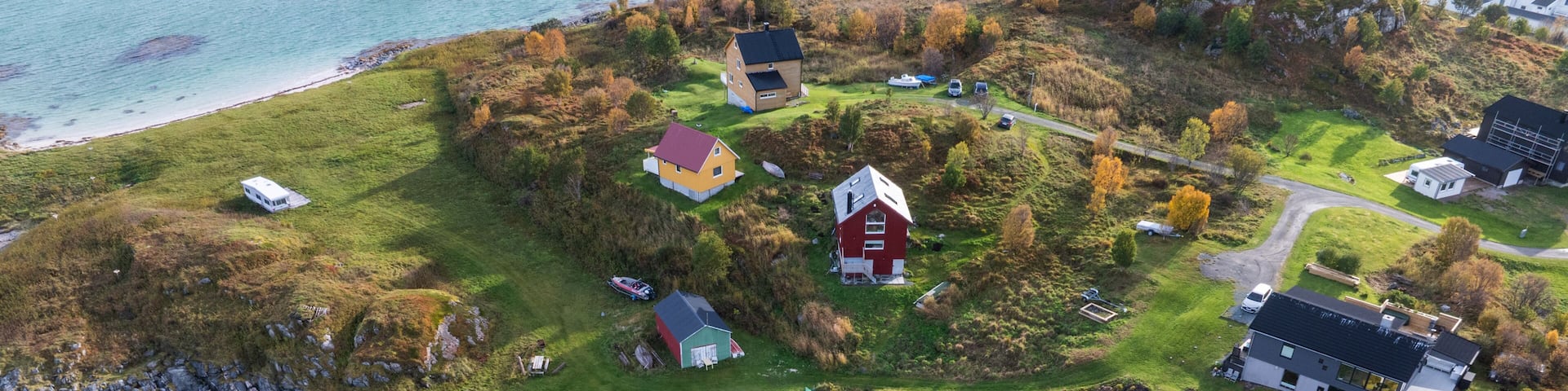Aerial view of colorful houses scattered on green hills overlooking a white sand beach and turquoise sea at Sommaroy, Troms, Norway.