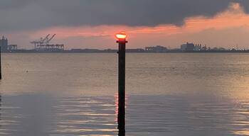 A sunset over a body of water with a pier and industrial structures in the background.