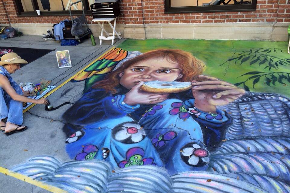 A street mural of a woman holding a donut, painted on a sidewalk.