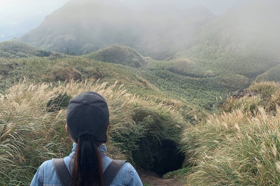 A person hiking on a grassy trail with hills and mountains in the background.