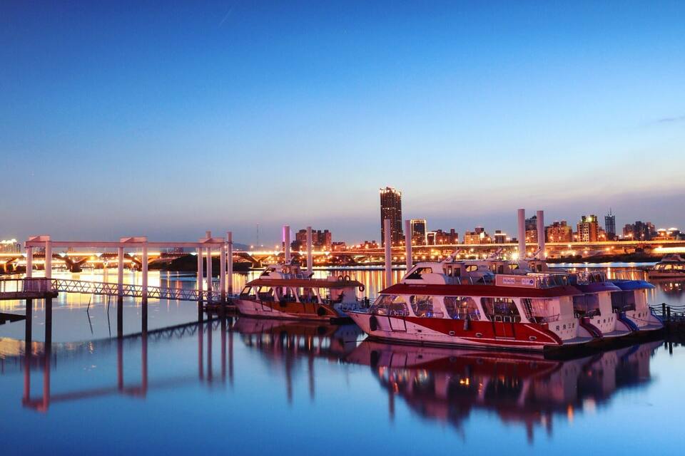 A marina at dusk with boats docked and a city skyline in the background.