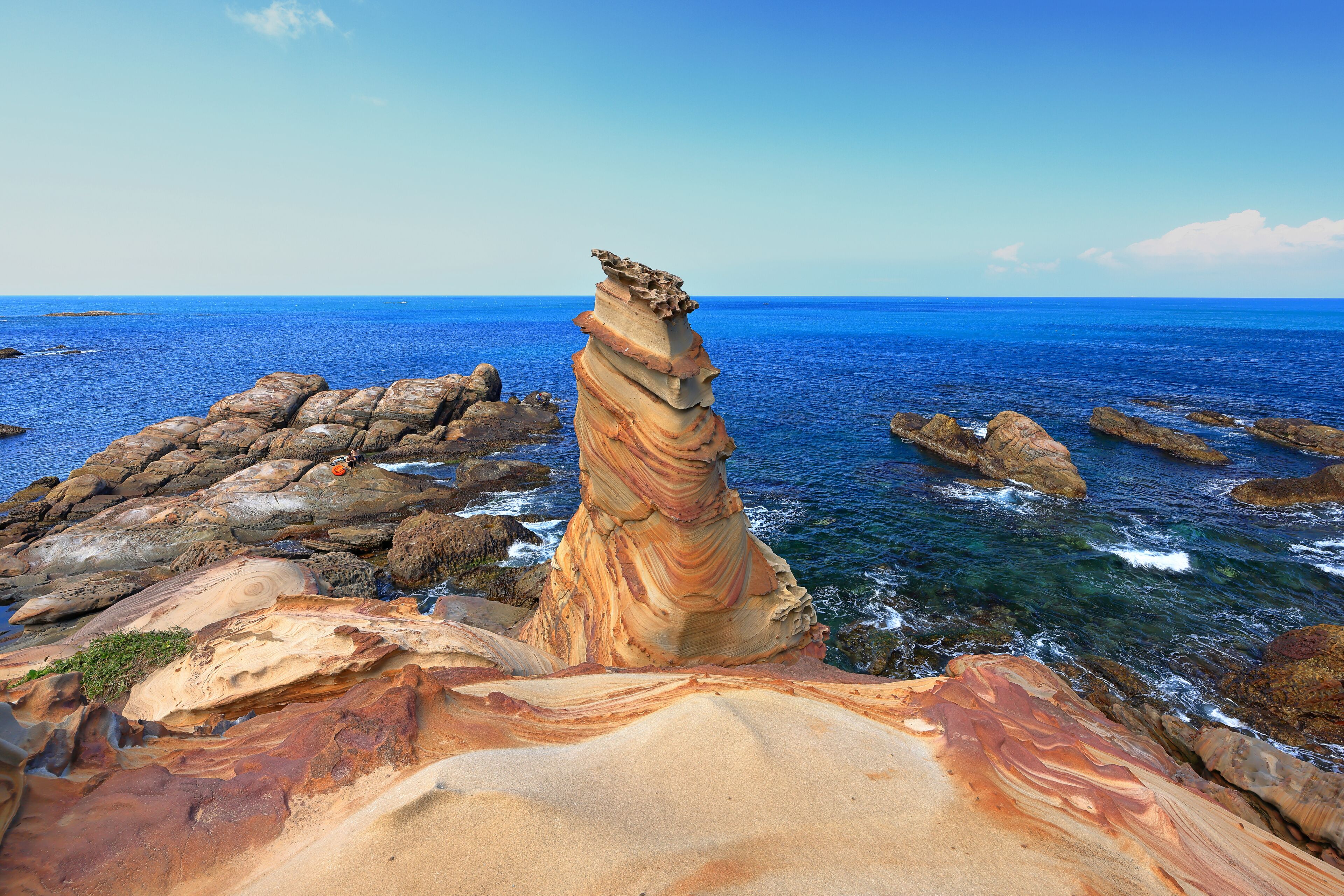 Formação rochosa costeira com camadas sedimentares e mar azul cristalino.