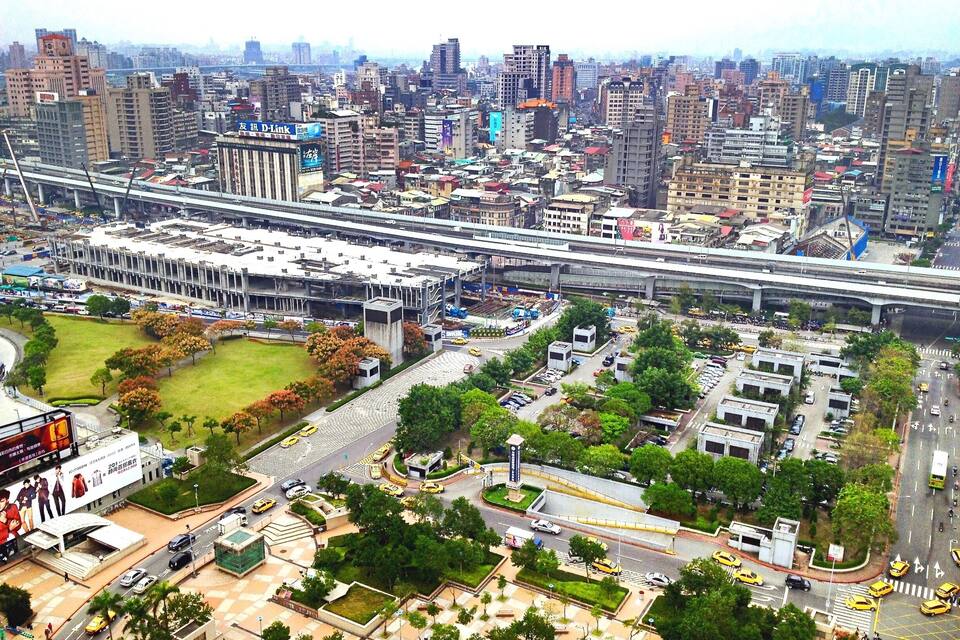 A cityscape with dense high-rise buildings, a large stadium, and a busy intersection with yellow taxis.