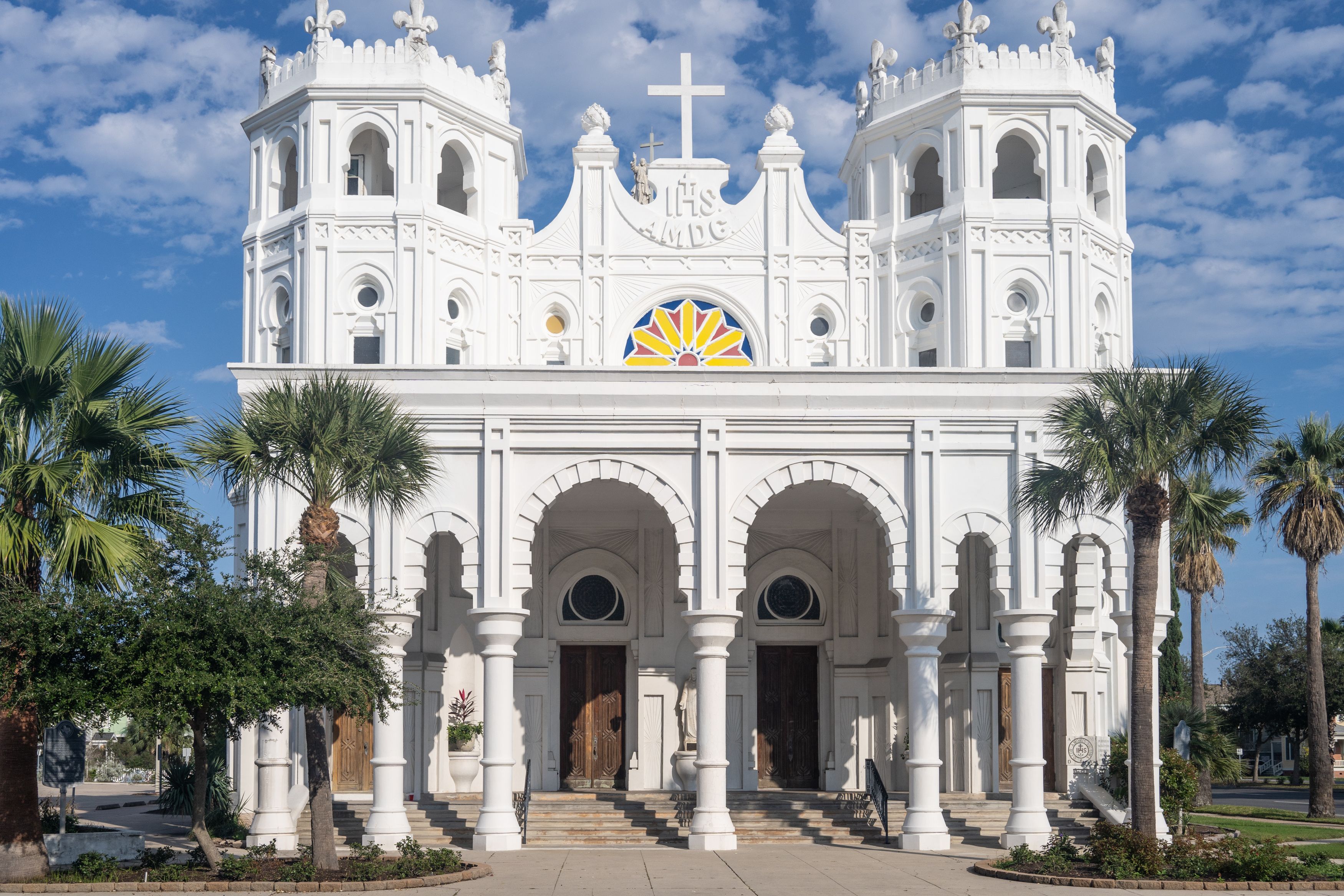 A white church with a cross, a colorful emblem, and palm trees.