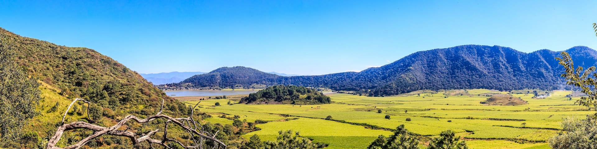 A valley with green fields, a lake, and mountains.