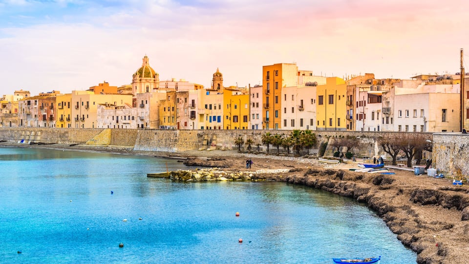 A coastal town with historic buildings, a calm harbor, and a small boat.