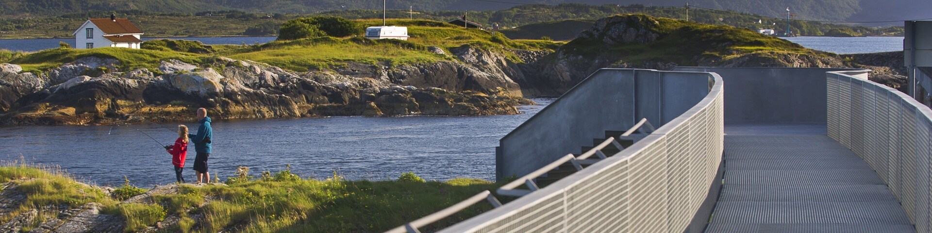 Uma ponte costeira com vista para uma montanha e uma pequena casa à beira-mar.
