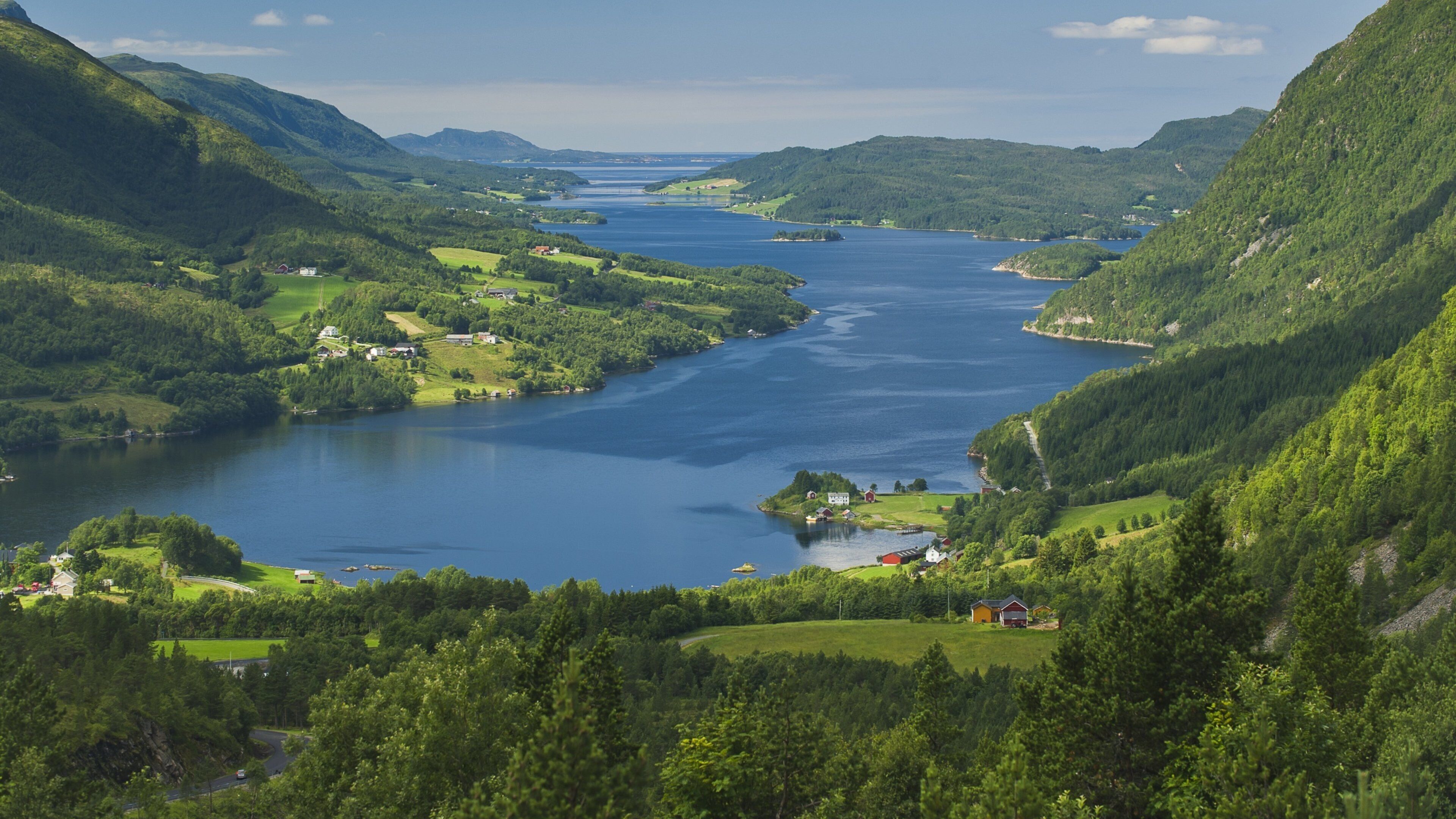 A river valley with lush greenery, a small island with buildings, and distant mountains.