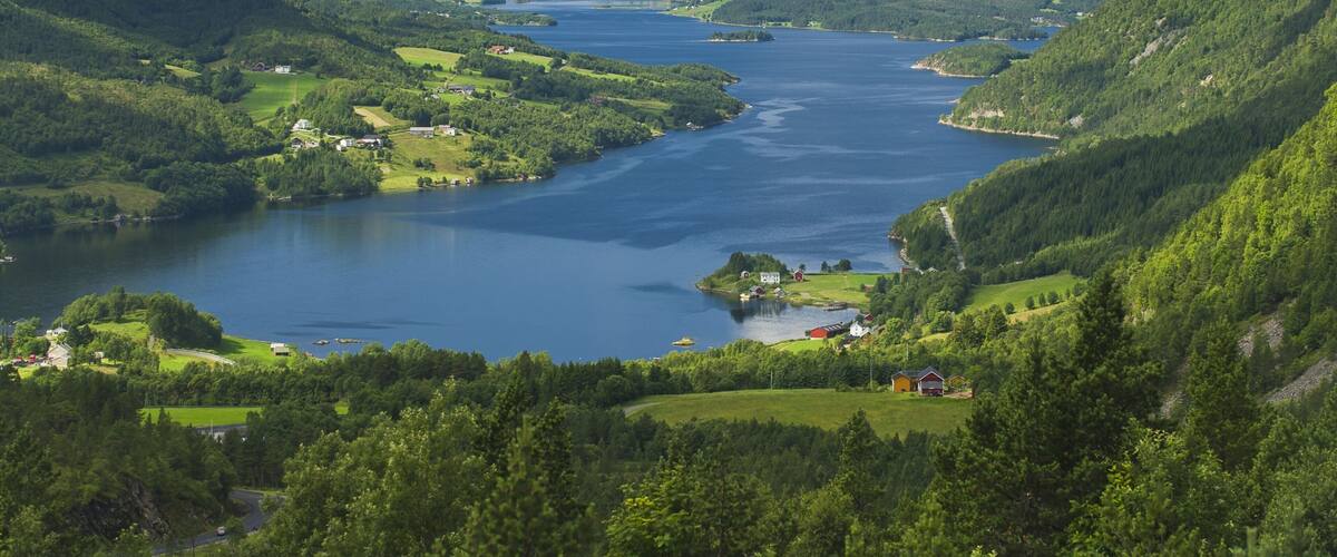 A river valley with lush greenery, a small island with buildings, and distant mountains.