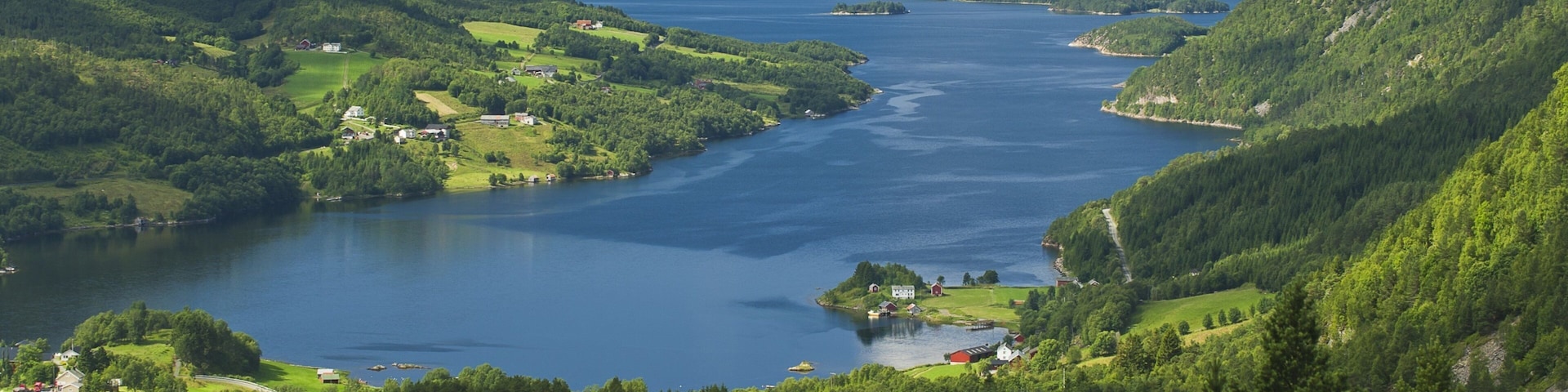 A river valley with lush greenery, a small island with buildings, and distant mountains.