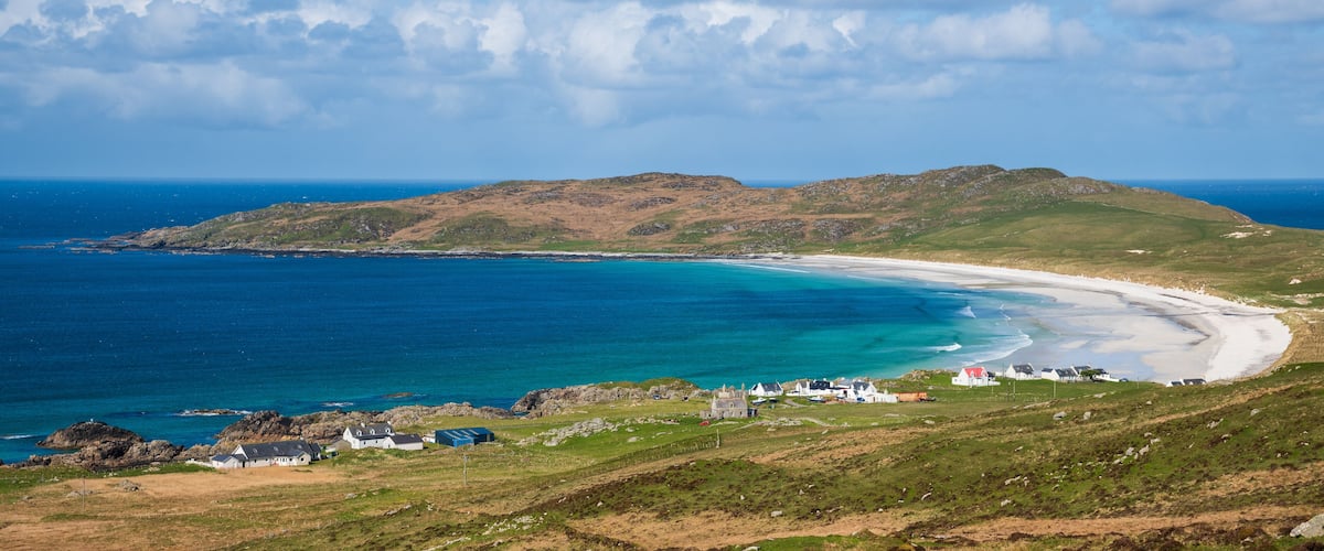 A coastal landscape with a sandy beach, rocky outcrops, and a grassy hill.