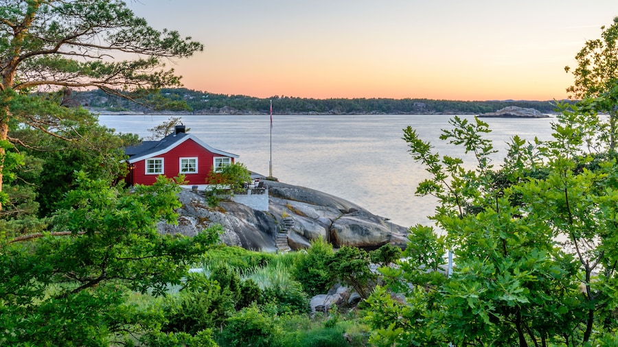 Sunset over the ocean shore, with a single red house, situated right on the coast