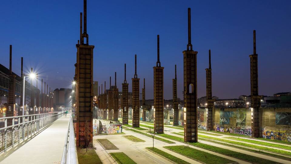 A nighttime view of a park with tall, rusted metal structures and graffiti-covered walls.