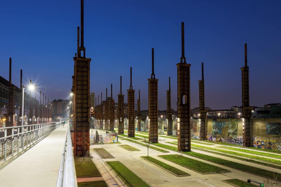 A nighttime view of a park with tall, rusted metal structures and graffiti-covered walls.