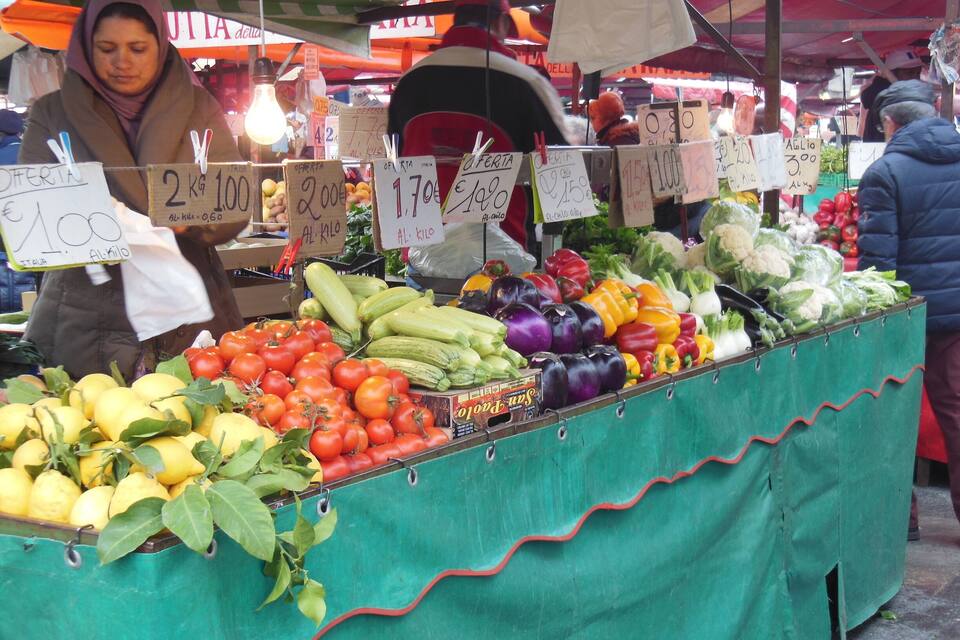 A market stall with various vegetables like tomatoes, cucumbers, and bell peppers.