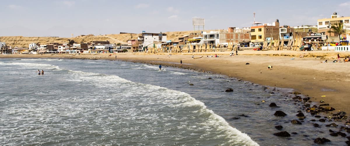 A coastal town with a sandy beach, rocky shoreline, and buildings along the shore.