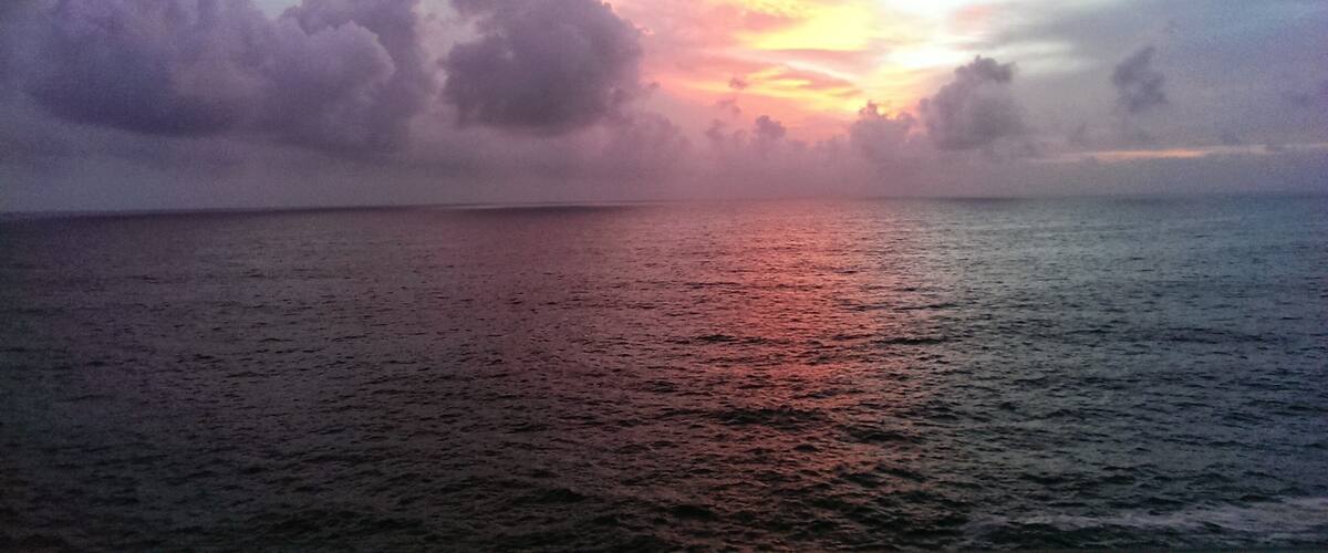 A sunset over a calm sea with scattered clouds.