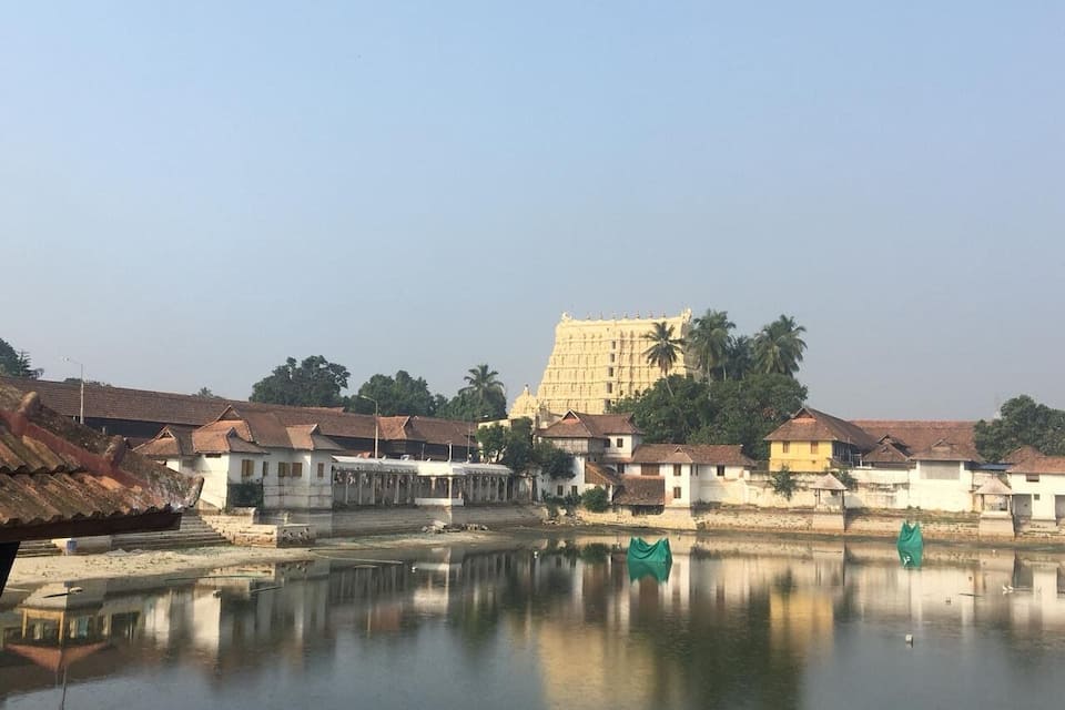 A calm river with reflections, traditional buildings, and a large temple in the background.
