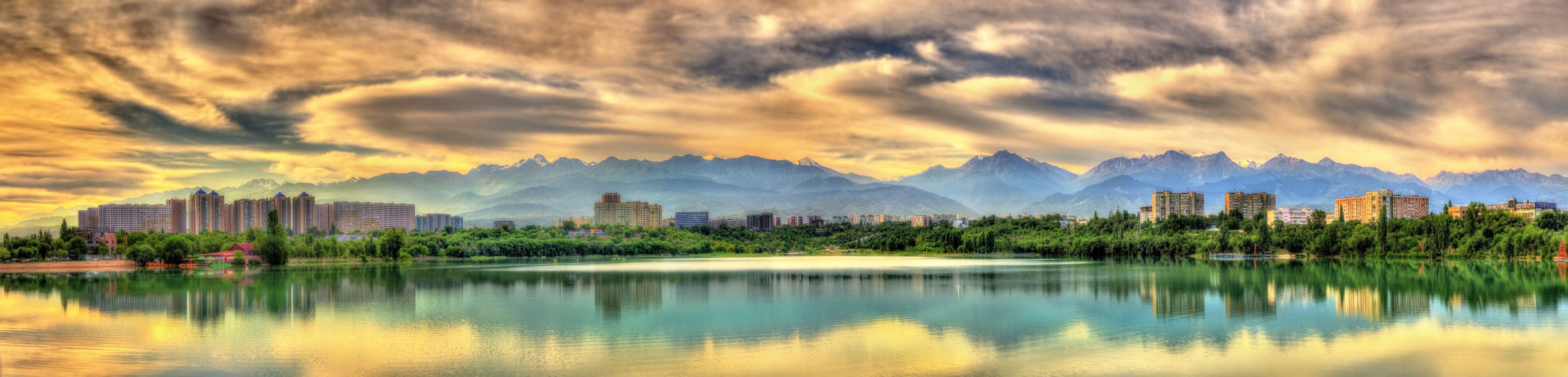 Un paisaje urbano con un río que refleja edificios, rodeado de montañas.
