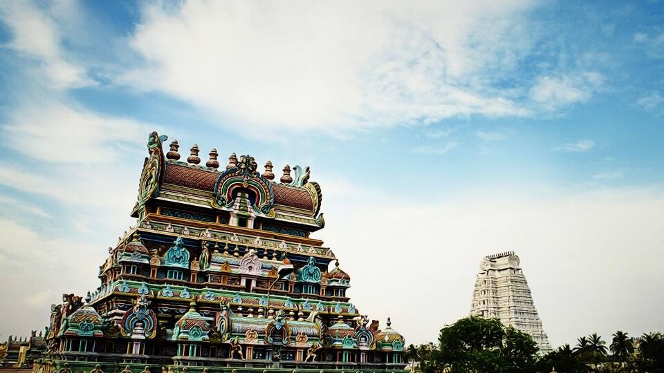 A colorful temple with intricate carvings and a tall tower in the background.