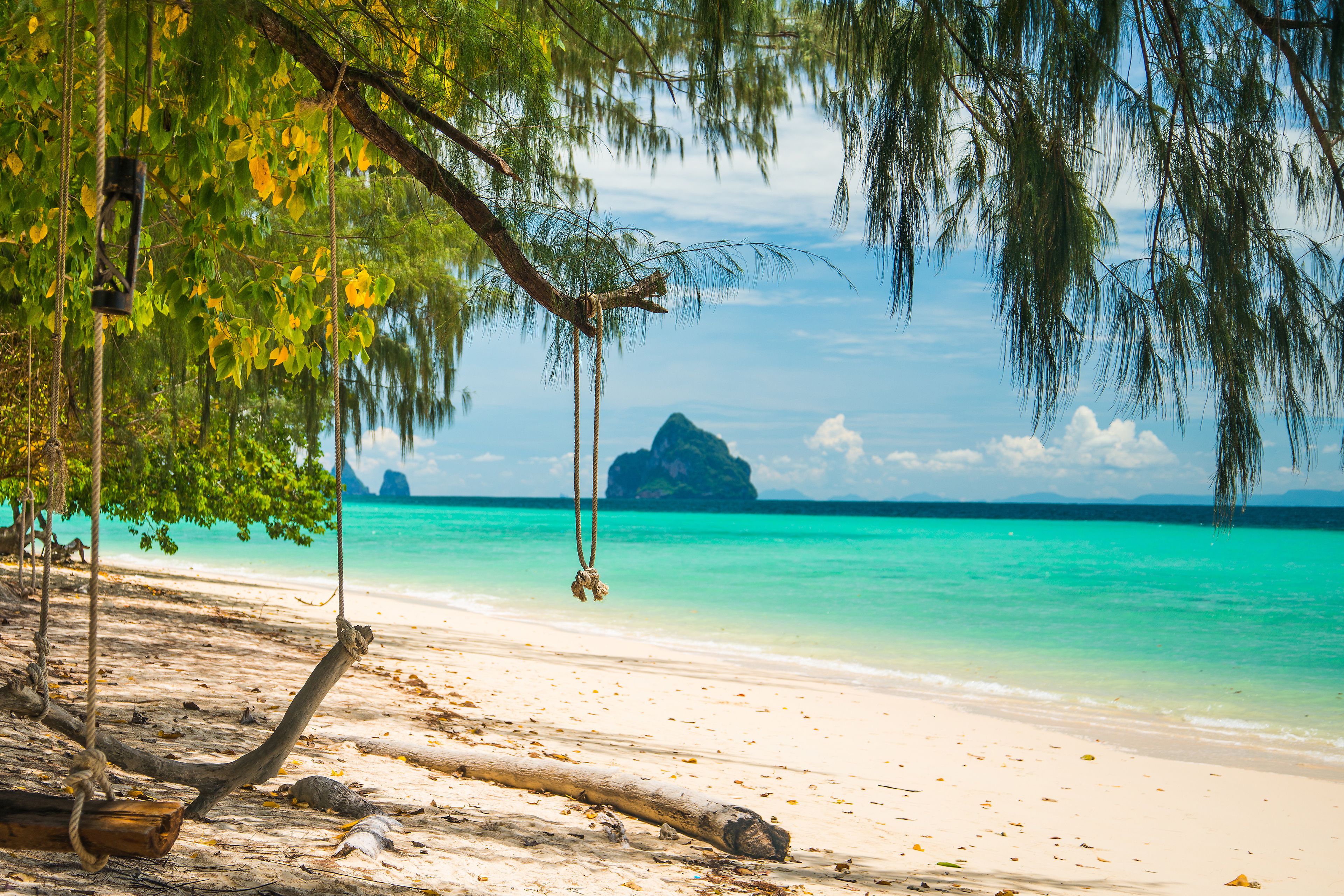 Una playa con agua turquesa cristalina, una hamaca colgada de un árbol y una montaña distante.