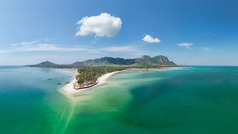 A tropical island with clear turquoise waters, a sandy beach, and a prominent mountain.